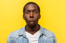 Portrait Of Excited Funny Man In Denim Shirt Making Fish Face With Lips And Big Amazed Eyes, Looking Surprised And Silly At Camera, Wondered Expression. Studio Shot Isolated On Yellow Background