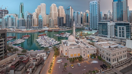 Yachts in Dubai Marina flanked by the Al Rahim Mosque and residential towers and skyscrapers aerial night to day timelapse.