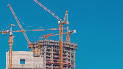 Aerial view of a skyscraper under construction with huge cranes timelapse in Dubai marina.