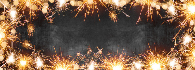 Silvester background banner panorama long- Frame made of sparklers and bokeh lights on rustic black concrete stone texture, top view with space for text