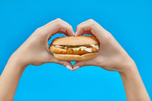 Woman Hands Holding A Burger On A Blue Background.  Two Hands Making Heart Sign With Hamburger