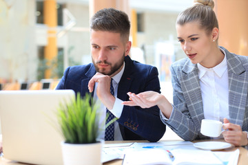 Two young business people using laptop in office while collaborating on startup project.