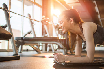 Wall Mural - Side view of beautiful sporty woman doing plank exercise on mat at gym