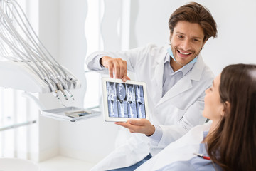 Handsome dentist showing his patient x-ray results, using digital tablet
