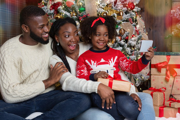 Wall Mural - Little afro girl taking selfie with her parents near Christmas tree