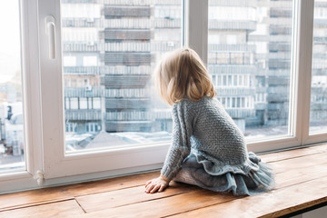 childhood concept. little girl sitting near window at home.