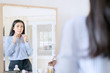 © Creativa Images - Elegant Asian businesswoman buttoning up shirt in front of mirror getting ready for work