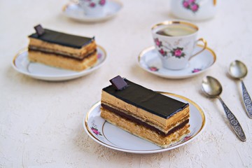 Sponge cake Opera, covered with chocolate, on a vintage dessert plate on a light background concrete. Classic desserts. Vintage dishes. French cuisine