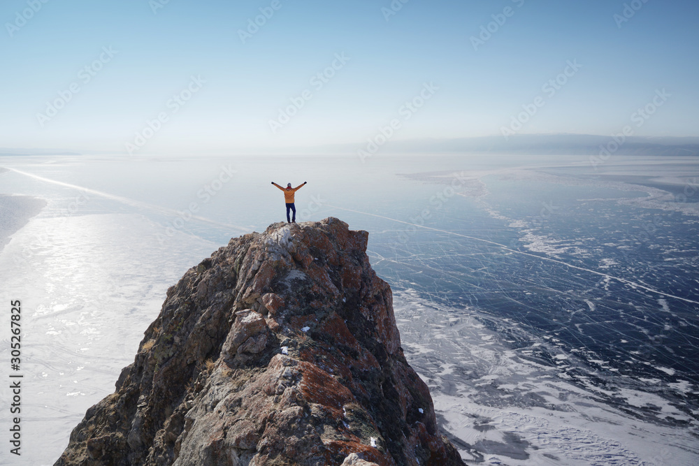 Lake Baikal at winter. Man standing on a cliff and looking at frozen Baikal lake. - obrazy, fototapety, plakaty 