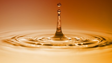 Wall Mural - Macro close up photo of water drop colliding and bouncing the surface in orange golden ambient light environment.