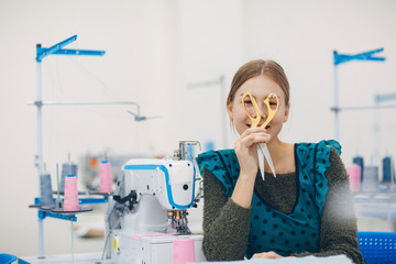 Young beautiful seamstress holding scissors on sewing machine in factory