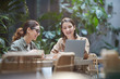 © Seventyfour - Portrait of two young women laughing happily while using laptop on outdoor cafe terrace decorated with plants, copy space