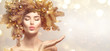 © Subbotina Anna - Christmas Woman with golden spruce tree wreath hairstyle on blurred pastel background. Beautiful Xmas model girl presenting hand, showing product, kiss. Hair style decorated, baubles. Christmas wishes