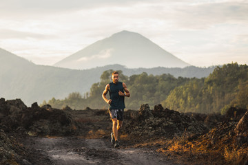 Wall Mural - Young athlete man trail running in mountains in the morning. Amazing volcanic landscape of Bali mount Agung on background. Healthy lifestyle concept.