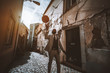 A fancy African man in an elegant formal suit with a necktie is spinning a basketball above him while standing on an antique narrow residential street with flaked walls in Lisbon, Portugal