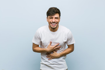 Wall Mural - Young caucasian man wearing a white tshirt laughs happily and has fun keeping hands on stomach.