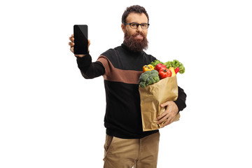 Wall Mural - Bearded man with a paper bag full of fruits and vegetables showing a mobile phone