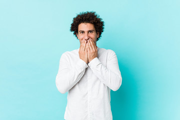 Young curly mature man wearing an elegant shirt laughing about something, covering mouth with hands.