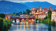Bridge Ponte degli Alpini at river Brenta Bassano del grappa Italy. Panoramic view at old town with vintage building and tower and wooden bridge at background Alpine mountains scenic landscape.