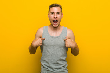 Wall Mural - Young caucasian sport man surprised pointing with finger, smiling broadly.