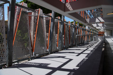 Perspective view of an interior walkway in a modern structure with railings, concrete beams, and perforated metal panels with orange trim