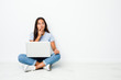 © Asier - Young mixed race indian woman sitting working on laptop looking sideways with doubtful and skeptical expression.