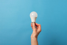 Female Hand Holds An LED Lamp On A Blue Background. Energy Saving Concept, Alternative Energy Sources, Idea