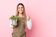 Young gardener woman holding a plant smiling and raising thumb up