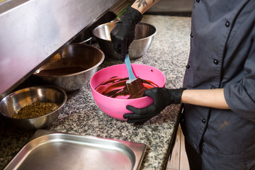 Theme cooking chocolate. Close-up of a hand. Young Caucasian woman cook with tattoo and in uniform prepares to make hot thick chocolate in a pot. Pastry chef mixes liquid chocolate in the kitchen