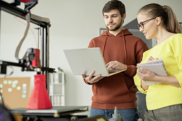 Canvas Print - Young engineer with laptop making presentation to his pretty colleague