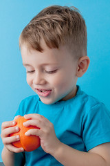 Wall Mural - Little Boy Holding an Orange in his hands on blue background, diet and exercise for good health concept