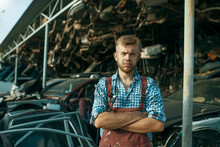 Male Mechanic At The Stack Of Cars On Junkyard