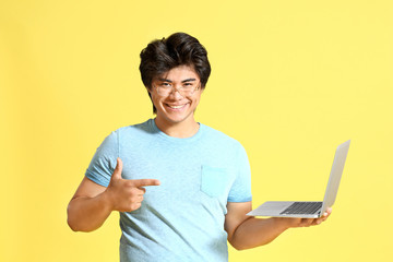 Male Asian programmer with laptop on color background