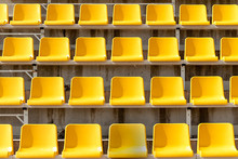 Yellow Seats On Stands Of Stadium In Open. Rows Are Horizontal. On Seats Shade From Sun. Front View.