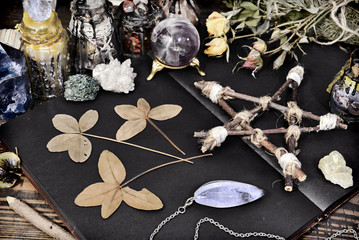 Creepy still life with open book, pentagram, four-lead clover and crystals on witch table.