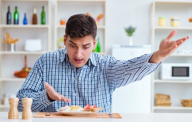 Wall Mural - Young husband eating tasteless food at home for lunch