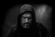Black And White Portrait Of A Bald Bearded Man In A Hood On A Dirty Gray Background