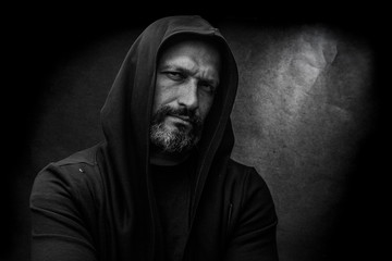 Black and white portrait of a bald bearded man in a hood on a dirty gray background