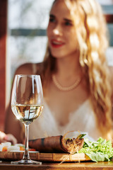 Wall Mural - Glass of white wine and appetizer on restaurant table in front of pretty young woman