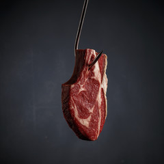 A piece of raw beef meat on a metal hook on a dark background