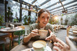 © Seventyfour - Fisheye view of smiling young woman holding coffee cup talking to friend across table in cafe, POV
