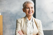 © shurkin_son - Success, employment, age and career concept. Portrait of attractive European mature female CEO in stylish beige suit posing at her office, keeping arms crossed on her chest, smiling confidently