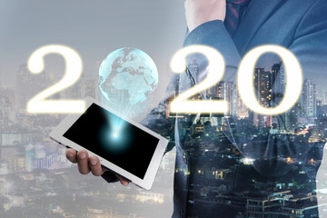 double exposure of businessmen using smart phone or tablet display hologram globe and 2020 text with blur city night and network connection concept