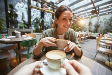 Fisheye View Of Smiling Woman Holding Coffee Cup Talking To Friend Across Table In Cafe, POV