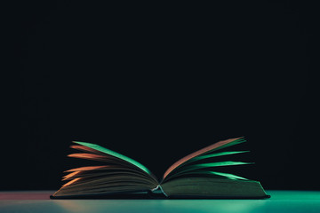 Fototapete - Beautiful open old book in the color light on a table and night background.