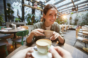 Fisheye view of smiling woman holding coffee cup talking to friend across table in cafe, POV