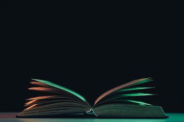 Fototapete - Beautiful open old book in the color light on a table and night background.