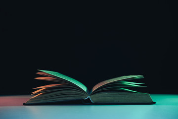 Fototapete - Beautiful open old book in the color light on a table and night background.