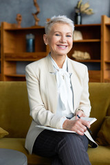 Wall Mural - People, age, career, profession and occupation concept. Vertical shot of cheerful mature woman entrepreneur having great idea, making plan or strategy for company, writing down in notebook, smiling