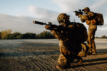Two Military Soldiers In Camouflage With Assault Rifles Looking Through The Scope Preparing To Attack At Sunset